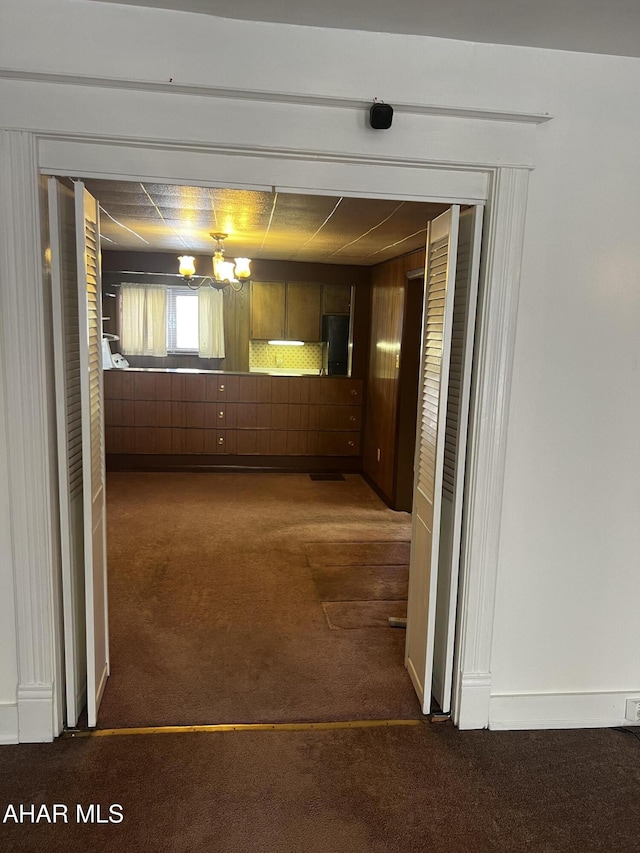 interior space with dark carpet, a chandelier, and wooden walls