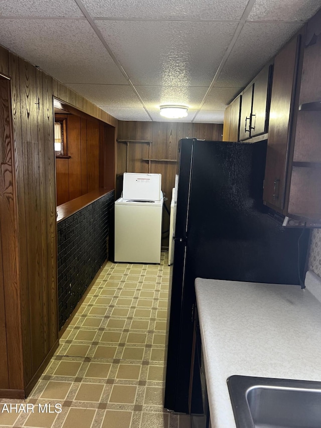 kitchen featuring washer / clothes dryer, wooden walls, and black fridge