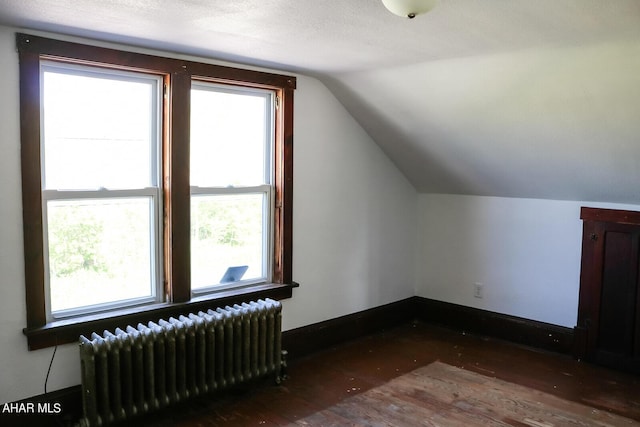 additional living space featuring radiator heating unit, dark hardwood / wood-style flooring, a textured ceiling, and vaulted ceiling