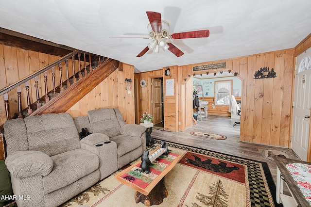 living room with hardwood / wood-style flooring, ceiling fan, and wooden walls