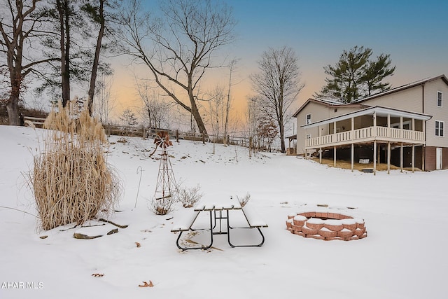 snowy yard with an outdoor fire pit and a sunroom