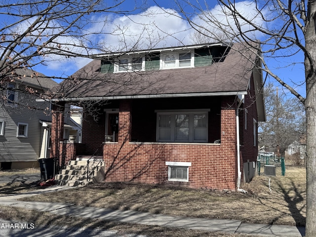 view of front of house featuring cooling unit, brick siding, and a shingled roof