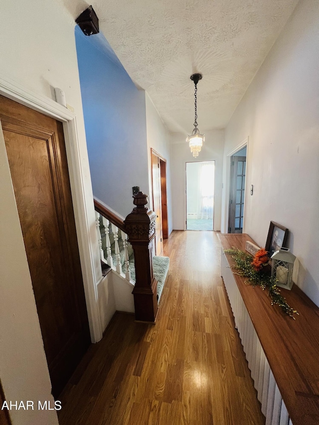 corridor with light hardwood / wood-style flooring, a chandelier, and a textured ceiling