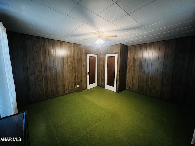 basement featuring carpet, ceiling fan, and wooden walls