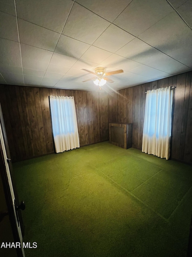 carpeted spare room with ceiling fan, a healthy amount of sunlight, and wood walls