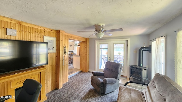 living room featuring a wood stove, wood walls, ceiling fan, and a textured ceiling