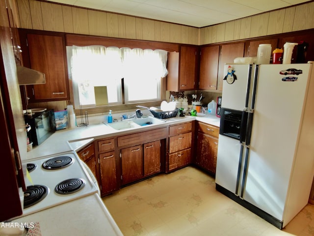 kitchen with white appliances, extractor fan, wood walls, and sink