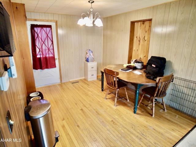 dining room featuring a notable chandelier, wood walls, and light wood-type flooring