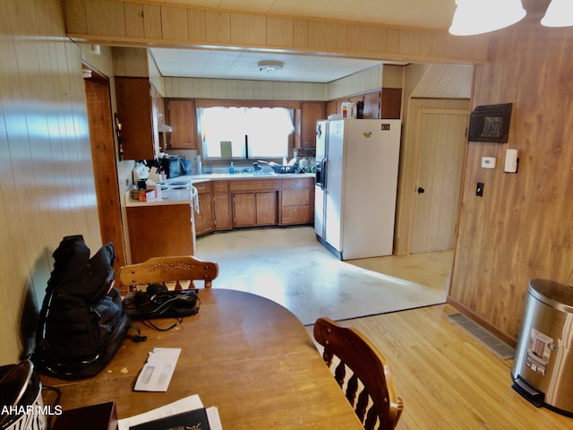 kitchen with wood walls, white appliances, and light hardwood / wood-style flooring