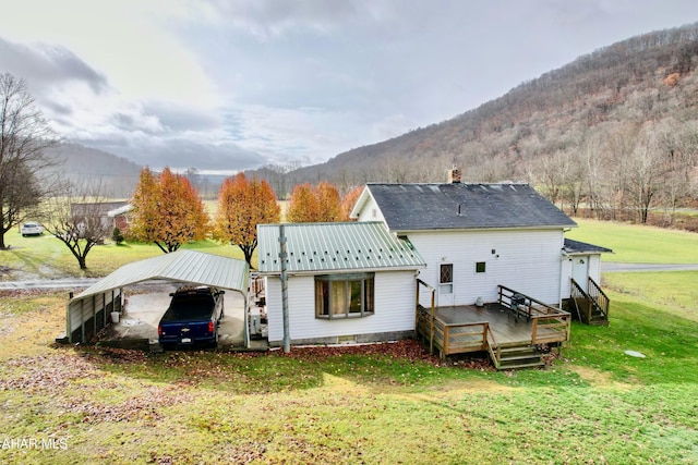 rear view of house with a yard, a deck with mountain view, and a carport