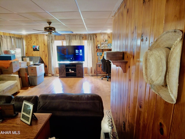 living room with a paneled ceiling, ceiling fan, light wood-type flooring, and wooden walls