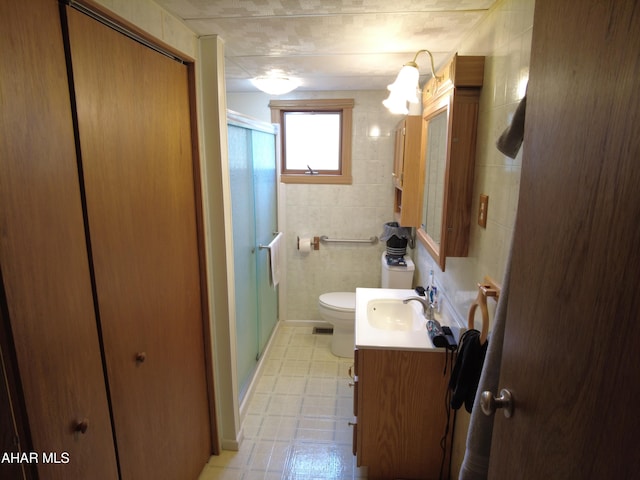 bathroom with vanity, toilet, a shower with shower door, and tile walls