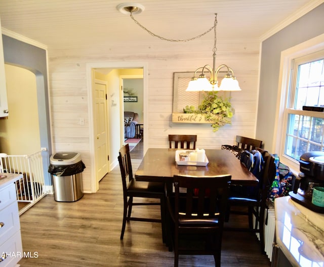 dining space featuring hardwood / wood-style flooring, crown molding, a notable chandelier, and wood walls