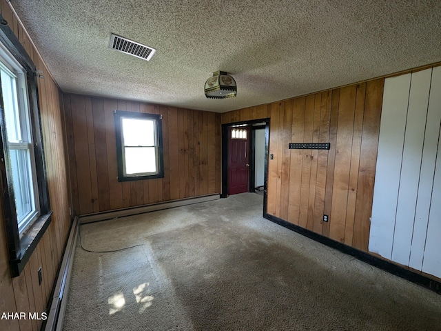 carpeted spare room featuring wood walls, a textured ceiling, and a baseboard radiator