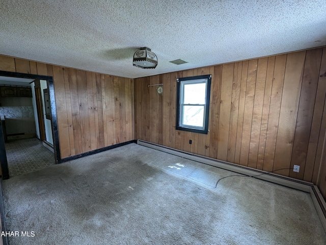 empty room with carpet floors, a textured ceiling, and wooden walls