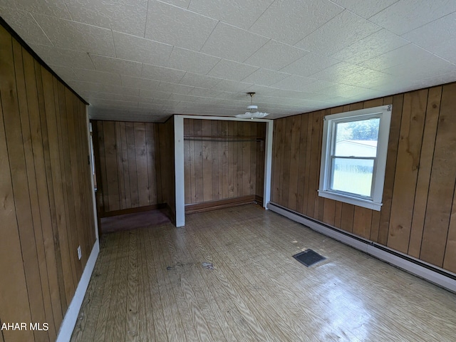 unfurnished bedroom with light wood-type flooring, a baseboard heating unit, and wood walls