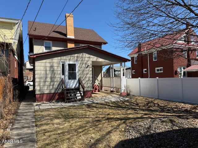 rear view of house with entry steps, fence, and a chimney