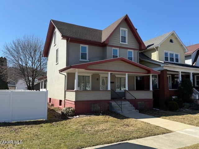 view of front of home featuring covered porch, a front lawn, and fence