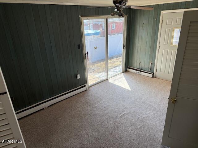 unfurnished room with baseboard heating, wood walls, ceiling fan, and carpet floors