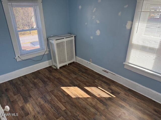 unfurnished room featuring radiator heating unit, baseboards, and dark wood-style flooring