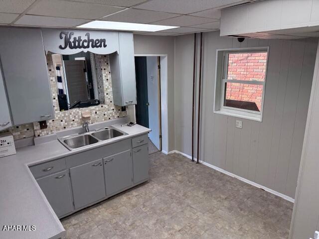 kitchen with a drop ceiling, light countertops, wooden walls, and a sink