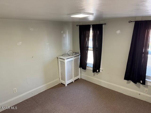 empty room featuring radiator, baseboards, and dark colored carpet