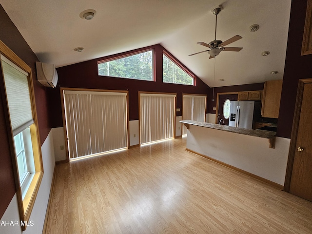 unfurnished living room featuring a wall unit AC, ceiling fan, high vaulted ceiling, and light wood-type flooring