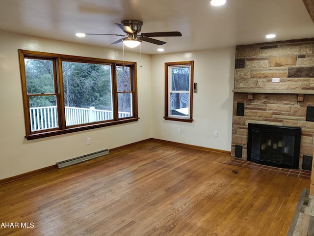 unfurnished living room with baseboard heating, a stone fireplace, ceiling fan, and wood-type flooring