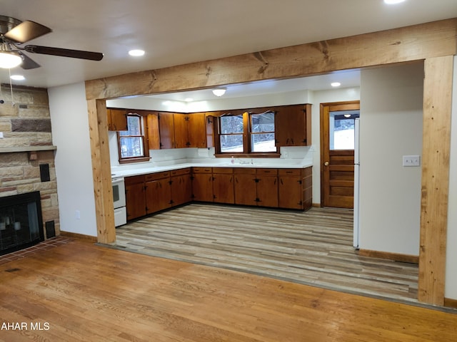 kitchen featuring stove, a stone fireplace, sink, ceiling fan, and light wood-type flooring