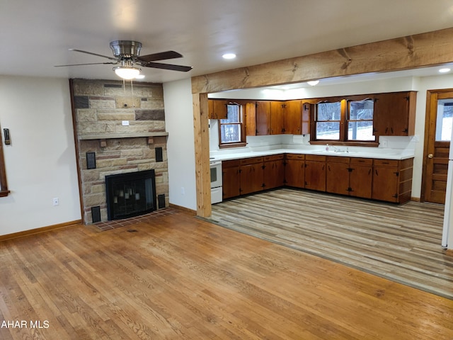 kitchen with stove, light wood-type flooring, ceiling fan, sink, and a stone fireplace