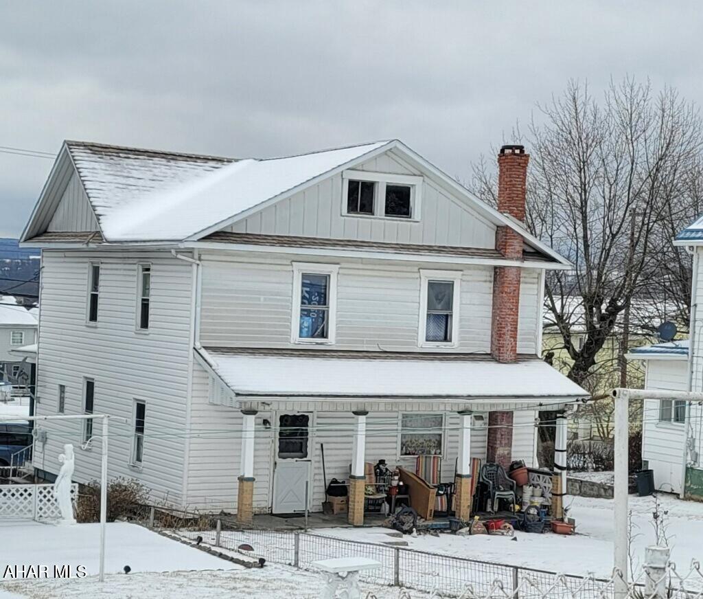 view of front facade featuring board and batten siding, covered porch, fence, and a chimney