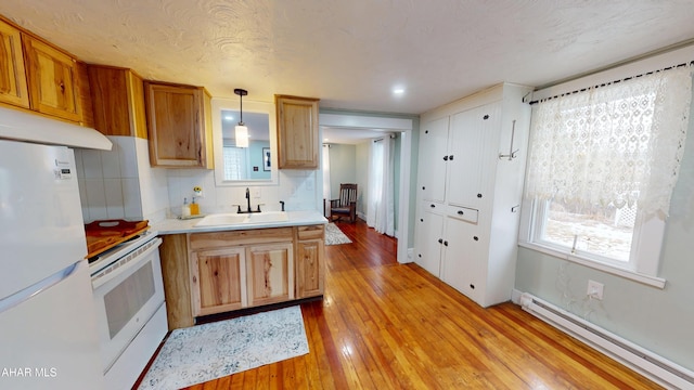 kitchen with light wood-style flooring, a baseboard heating unit, white appliances, a sink, and light countertops