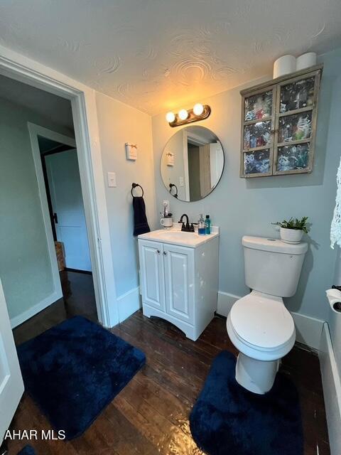 bathroom featuring toilet, baseboards, wood finished floors, and vanity