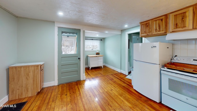 kitchen with light wood finished floors, brown cabinetry, white appliances, under cabinet range hood, and baseboards