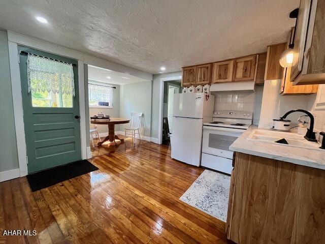 kitchen featuring white appliances, dark wood-style flooring, light countertops, under cabinet range hood, and a sink