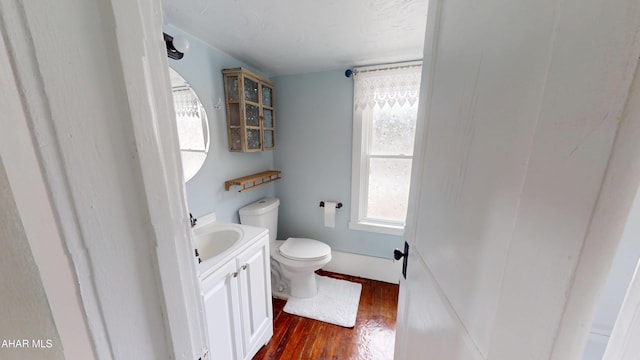 half bath with toilet, wood finished floors, and vanity