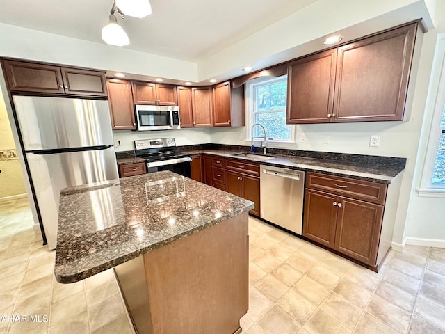 kitchen featuring appliances with stainless steel finishes, a kitchen breakfast bar, dark stone counters, sink, and a kitchen island