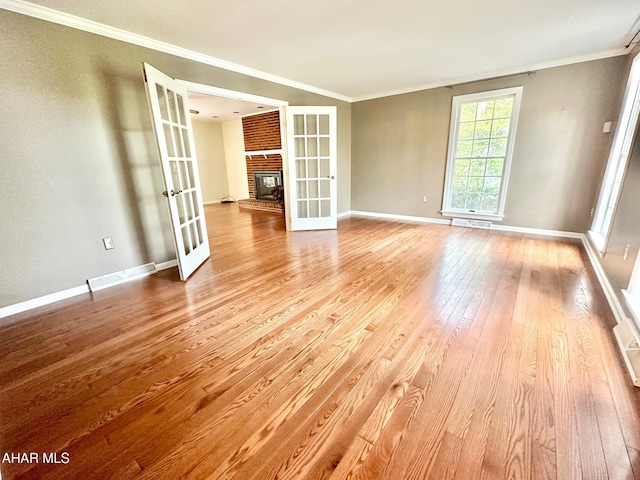 unfurnished room with a fireplace, french doors, light hardwood / wood-style floors, and ornamental molding