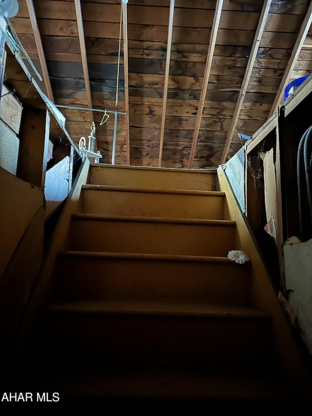 staircase with wooden walls, wooden ceiling, and vaulted ceiling