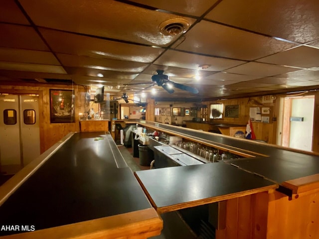 game room with wooden walls, a drop ceiling, and ceiling fan