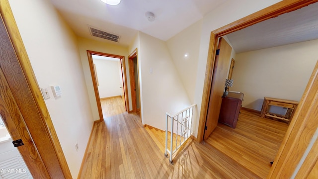 hall with an upstairs landing, visible vents, light wood-type flooring, and baseboards