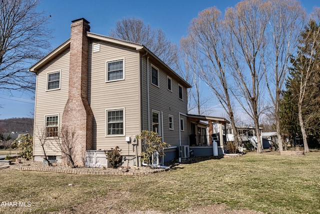 rear view of property featuring a lawn, central AC unit, covered porch, and a chimney