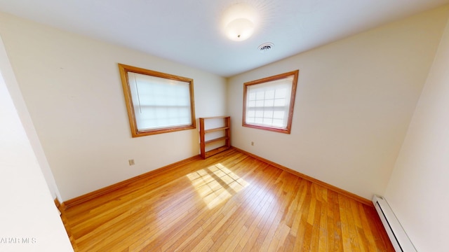 empty room featuring baseboards, visible vents, light wood finished floors, and a baseboard radiator