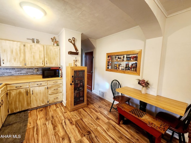 kitchen with visible vents, light wood finished floors, ornamental molding, black microwave, and backsplash