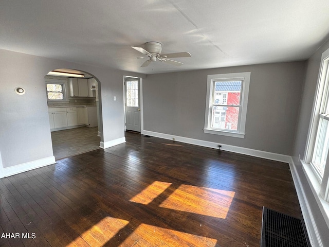 unfurnished room featuring arched walkways, dark wood-style flooring, plenty of natural light, and visible vents