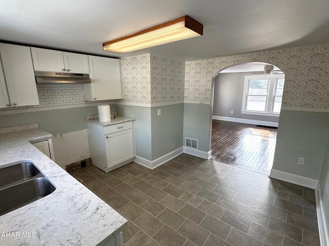 kitchen featuring wainscoting, white cabinets, under cabinet range hood, and wallpapered walls