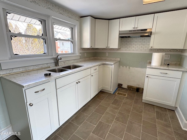 kitchen with under cabinet range hood, white cabinetry, and a sink