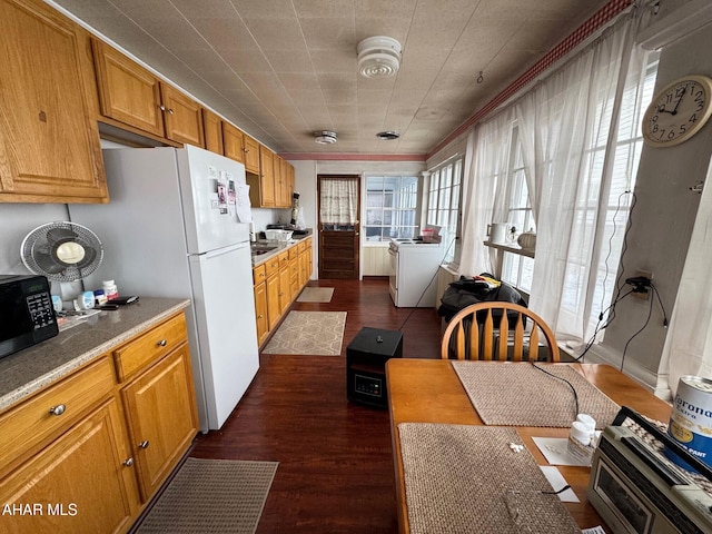 kitchen featuring dark wood finished floors, light countertops, brown cabinetry, washer and dryer, and black microwave