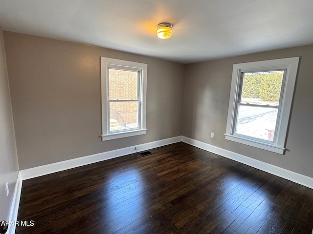 empty room with dark wood-type flooring, visible vents, and baseboards