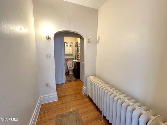 hallway with radiator, light wood-style floors, baseboards, and arched walkways